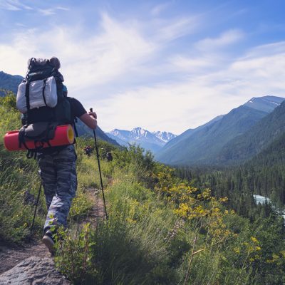 Man hiking at sunset mountains with heavy backpack Travel Lifestyle wanderlust adventure concept summer vacations outdoor alone into the wild. Nordic walking sticks